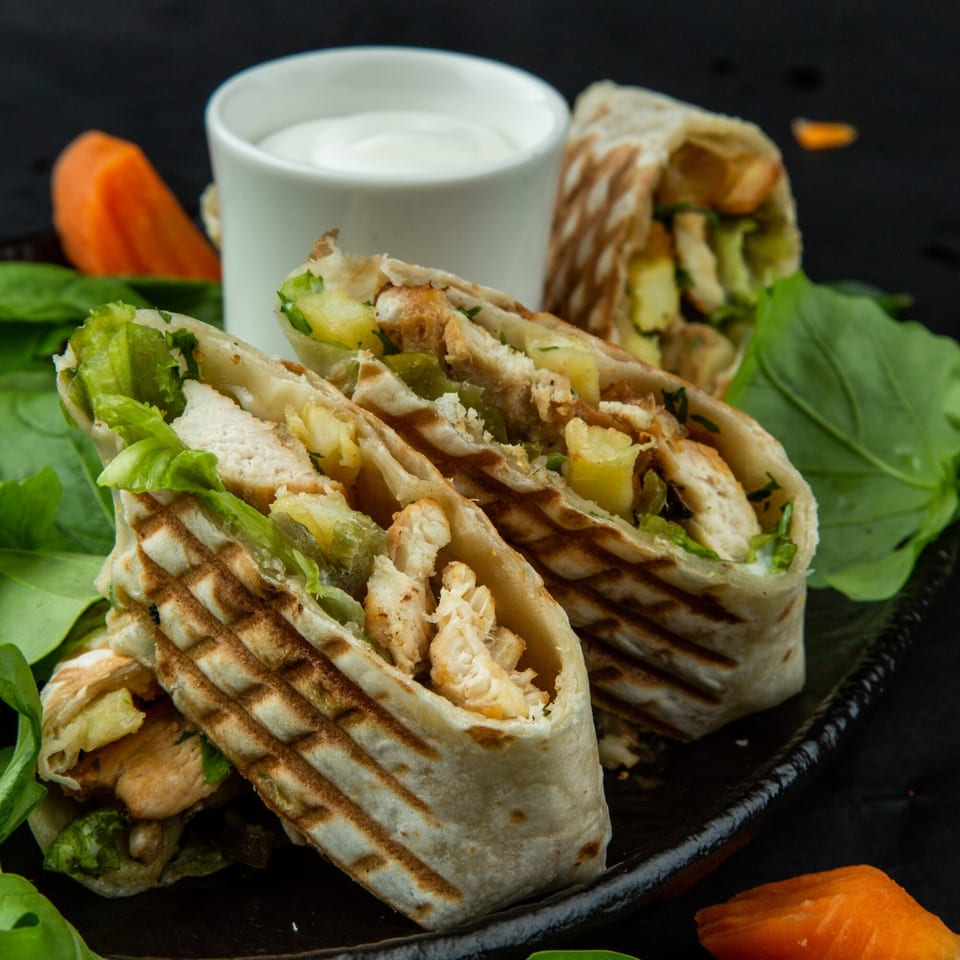 Grilled chicken wraps with lettuce and pineapple, served with a side of white sauce.