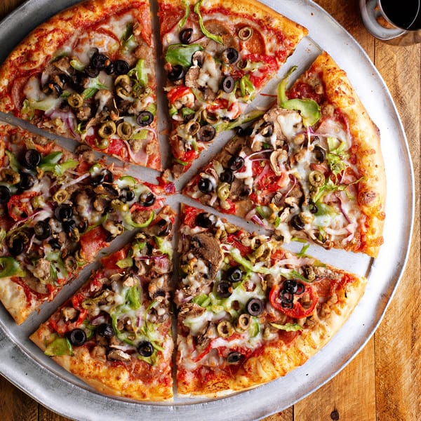 A Runner Pizza Stoughton pizza, cut into slices, with various toppings on a metal tray.