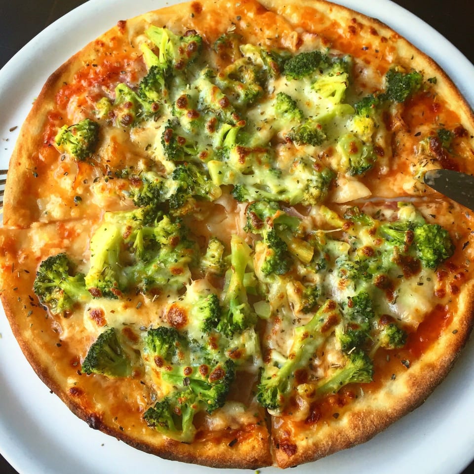 Runner Pizza Stoughton's broccoli pizza, topped with melted cheese and herbs, with one slice removed.