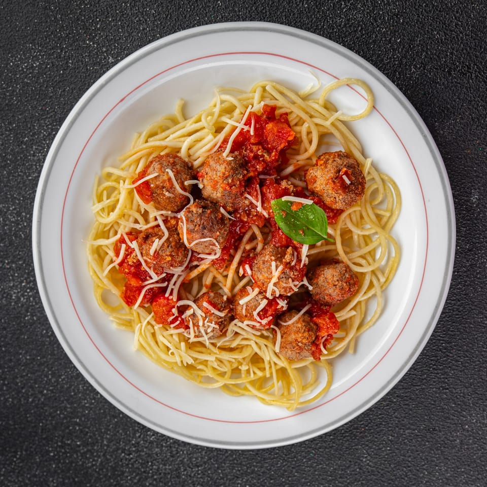 Spaghetti with meatballs, tomato sauce, grated cheese, and a basil leaf on a white plate.